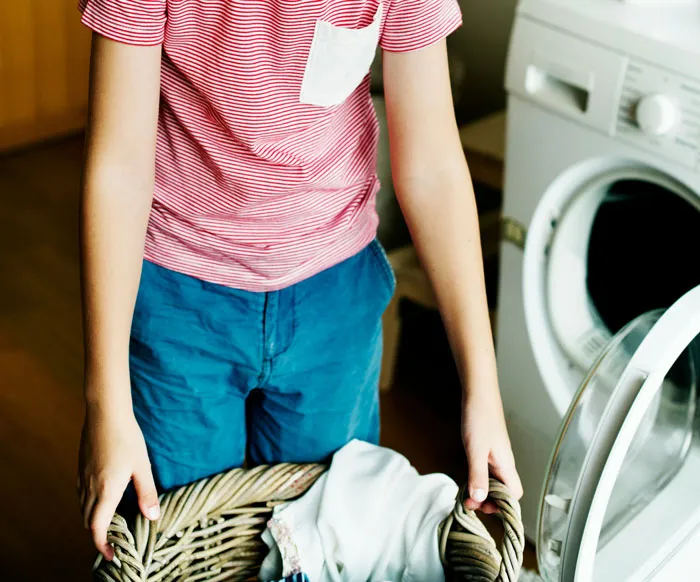 Child holding laundry basket near washing machine, capturing a relatable moment of instant karma in everyday chores.