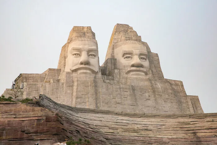 Massive stone sculpture of two bearded men carved into a mountain, a spectacular sculpture attracting global travelers.