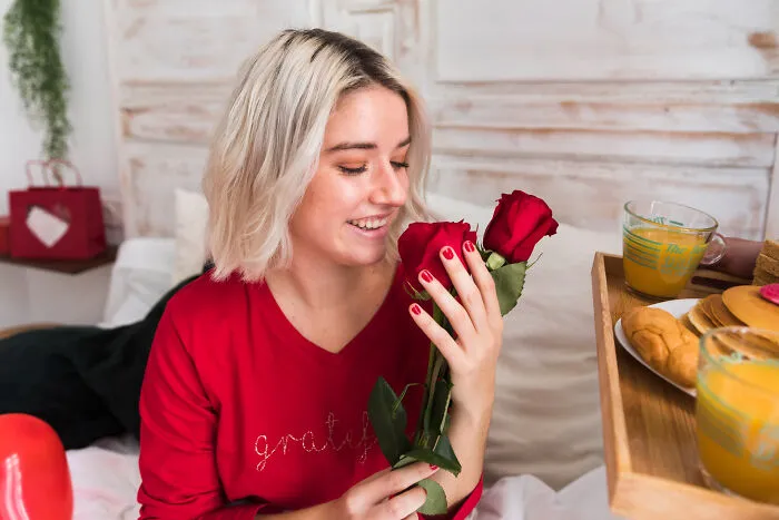 Young woman in red shirt smiling while holding red roses, illustrating little lie that backfired on them hard concept.