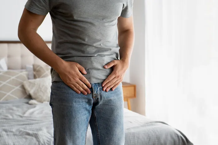 Man standing by bed holding stomach in pain, illustrating discomfort from a little lie that backfired hard.