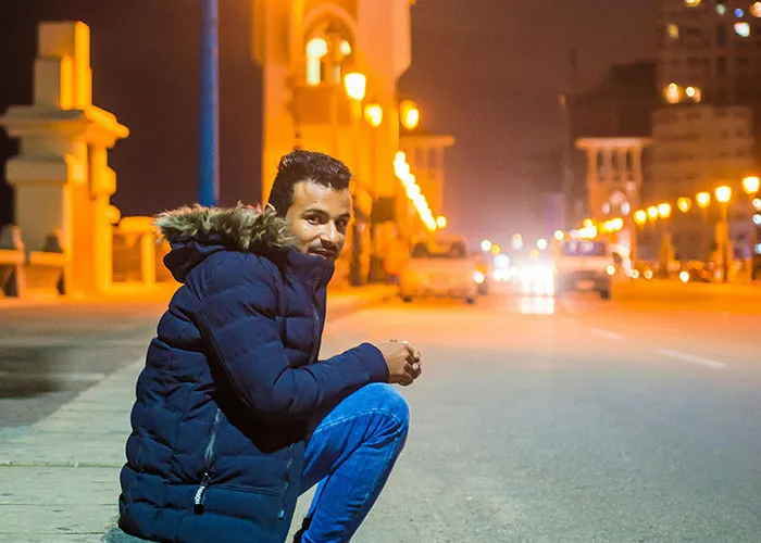 Man in a blue jacket sitting on a city street at night in one of the worst cities worldwide to avoid visiting.