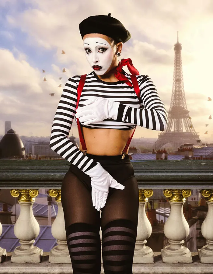 Mime artist in striped costume and white gloves posing in front of the Eiffel Tower as part of Halloween costumes by celebrities