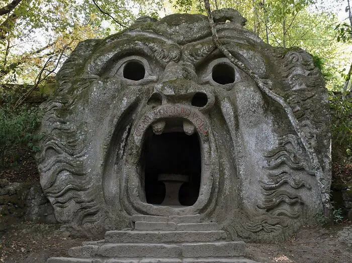 Stone sculpture of a giant face with an open mouth entrance surrounded by trees, a spectacular travel attraction.