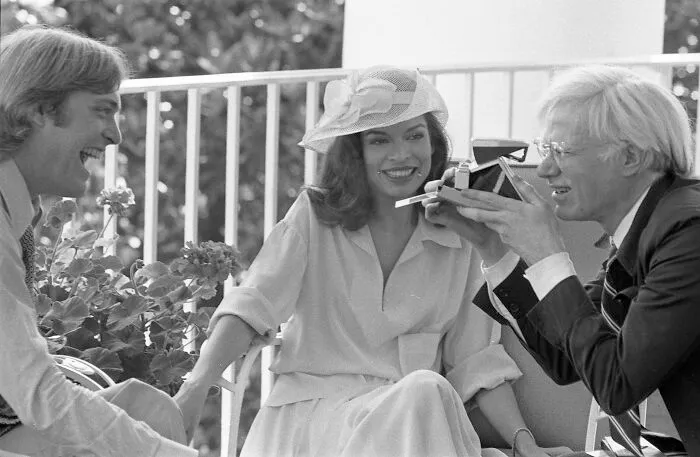 Three style icons in vintage fashion, smiling and interacting with a camera on a sunny outdoor terrace.