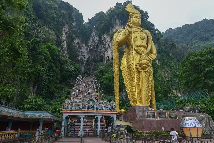 Golden statue sculpture at the entrance of Batu Caves, a spectacular travel bucket list destination surrounded by lush greenery.