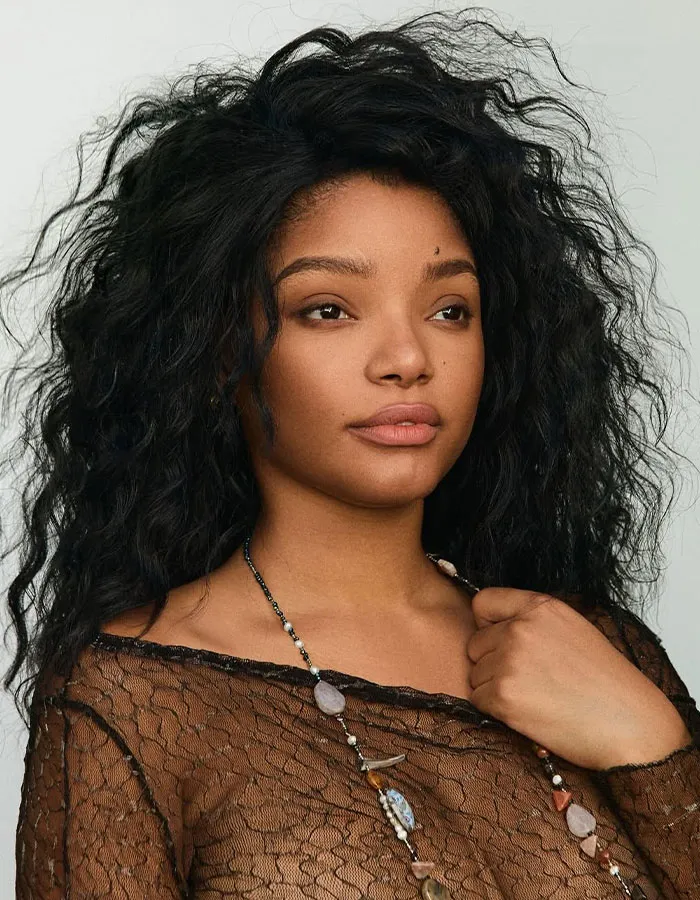 Young woman with voluminous curly hair wearing a lace top and gemstone necklace, showcasing celebrity Halloween costumes.