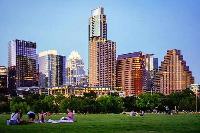 City skyline with groups of people relaxing on grass, illustrating places solo female travelers do not recommend.