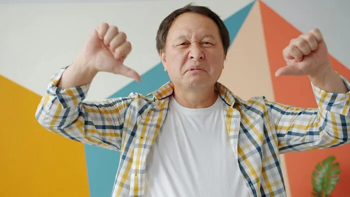 Middle-aged man showing thumbs down with a displeased expression representing toxic relationship traits concept