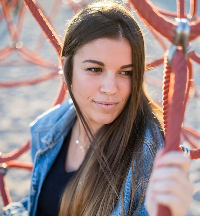 Young woman with long hair and denim jacket holding a red rope structure, symbolizing unhinged behavior and relationships.