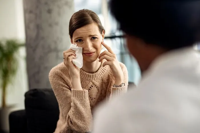 Woman wiping tears talking to a doctor, illustrating insensitive things said to people having a hard time with cancer.