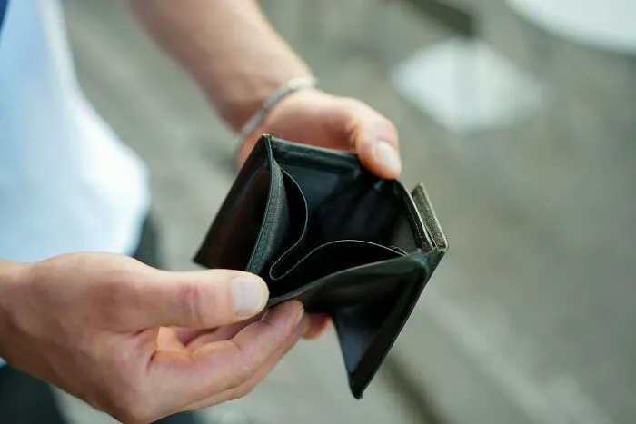 Person holding an empty wallet, illustrating financial loss after falling for scams and how it affected them.