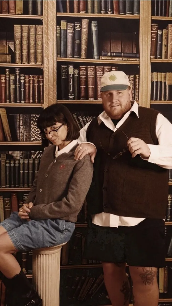 Pareja posando con estilo informal frente a una biblioteca, representando fallos en fotos familiares virales en internet.