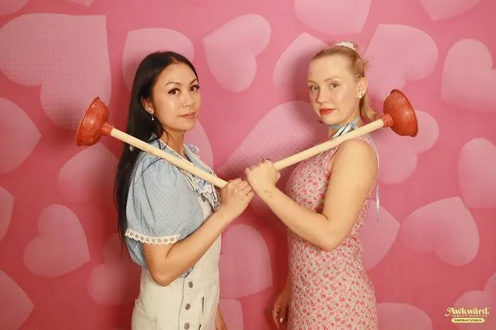Dos mujeres posando con desatascadores cruzados, imagen divertida de fallos en fotos familiares para internet.