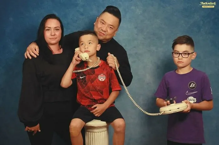 Foto familiar con error divertido donde un niño sostiene un teléfono antiguo mientras todos posan juntos para la cámara.
