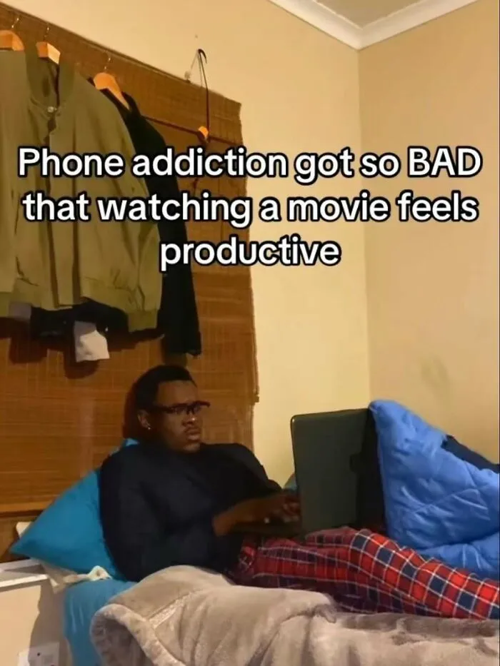 Person in pajamas lying on bed using a laptop with a meme about phone addiction to fight boredom and sadness.