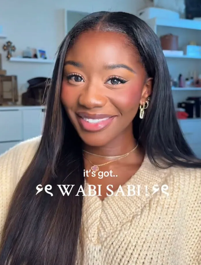Smiling woman with long hair and gold earrings, embracing perfect imperfections in a wholesome trend about self-acceptance.