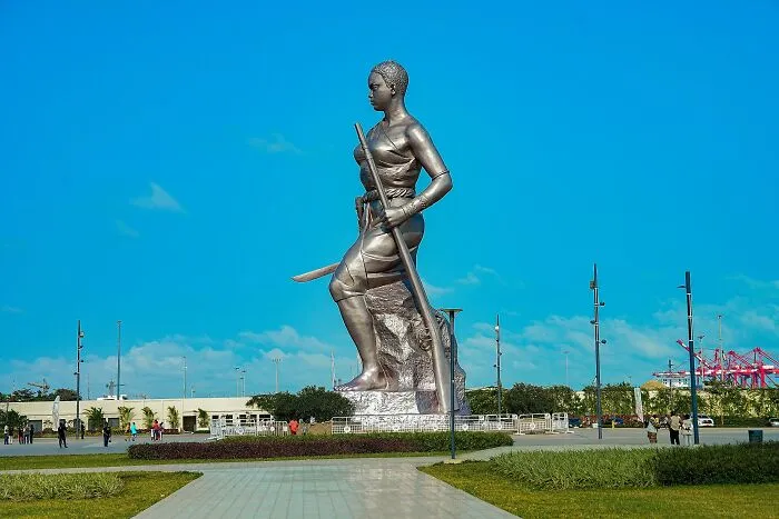 Large spectacular sculpture of a woman holding a spear and sword in an open plaza under a clear blue sky.