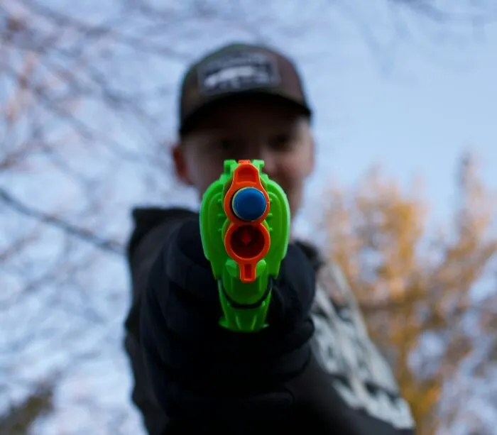 Child pointing a toy gun towards the camera, capturing a funny and serious moment raising monsters outdoors.