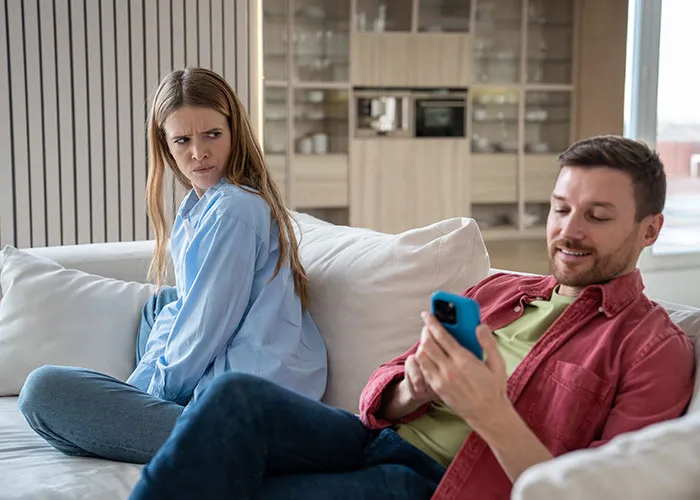 A woman giving a suspicious look to a man on his phone, depicting wild family drama moments at home.