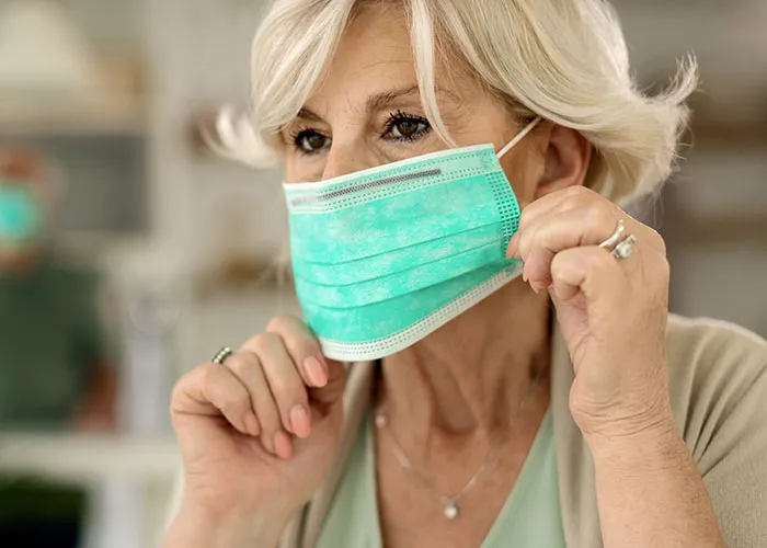 Older woman adjusting a surgical mask indoors, highlighting themes of wild family dramas and relatable family dynamics.