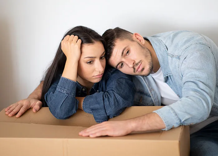 A young couple looking distressed and leaning on a cardboard box, illustrating wild family dramas and tense relationships.