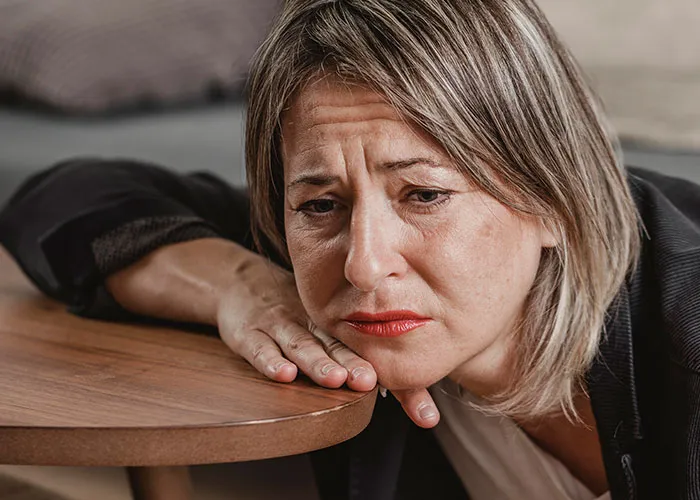 Woman with worried expression resting head on hand near wooden table, reflecting on wild family dramas and difficult relatives.