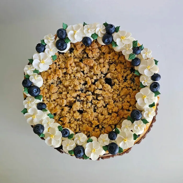 Blueberry crumb cake decorated with white frosting flowers and fresh blueberries showcasing gorgeous baked goods.