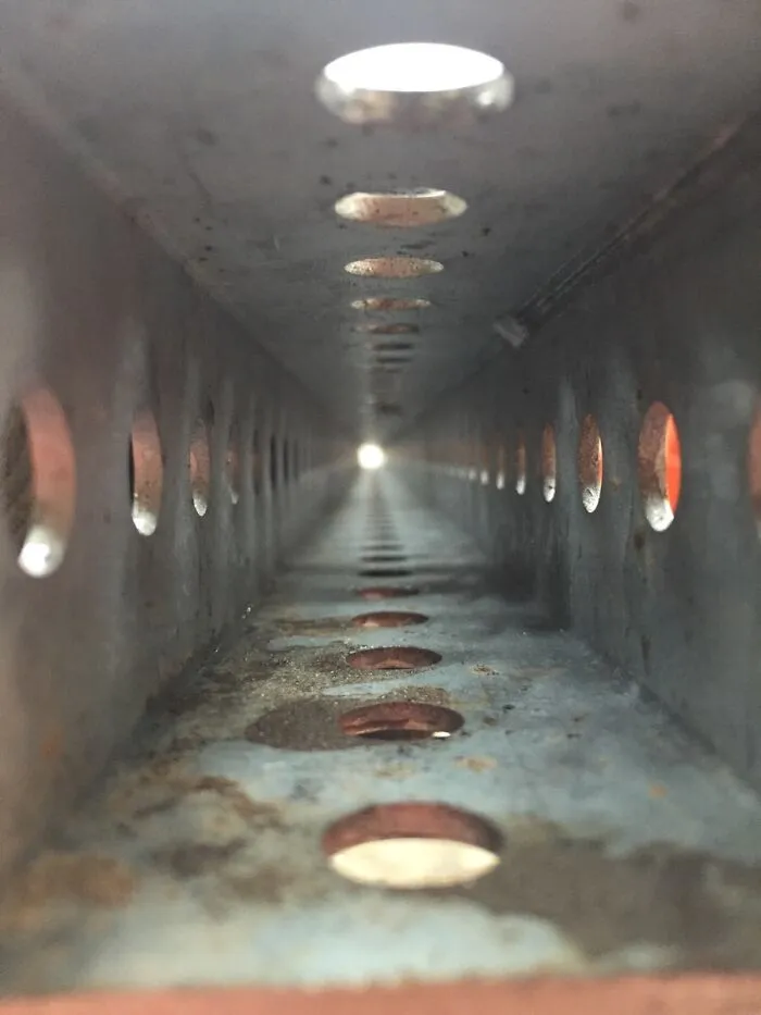 Close-up of the insides of a rusty perforated metal beam showing depth and light at the far end.