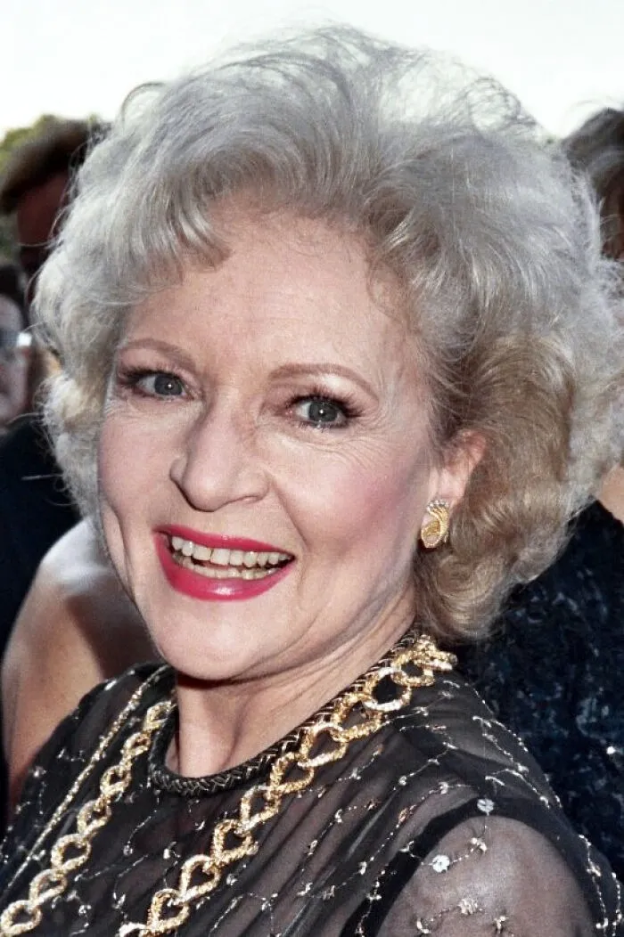 Older woman with curly gray hair and red lipstick smiling at event, representing Hollywood stars who found fame after 30.