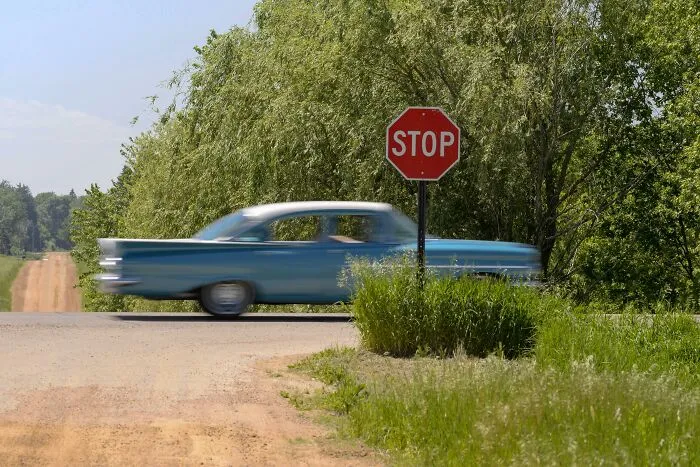 Blue vintage car speeding past a stop sign on a rural road with trees, illustrating interesting laws and legal loopholes.