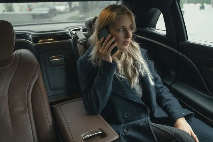 Woman in a dark coat sitting in a car interior, talking on the phone about interesting laws and legal loopholes.