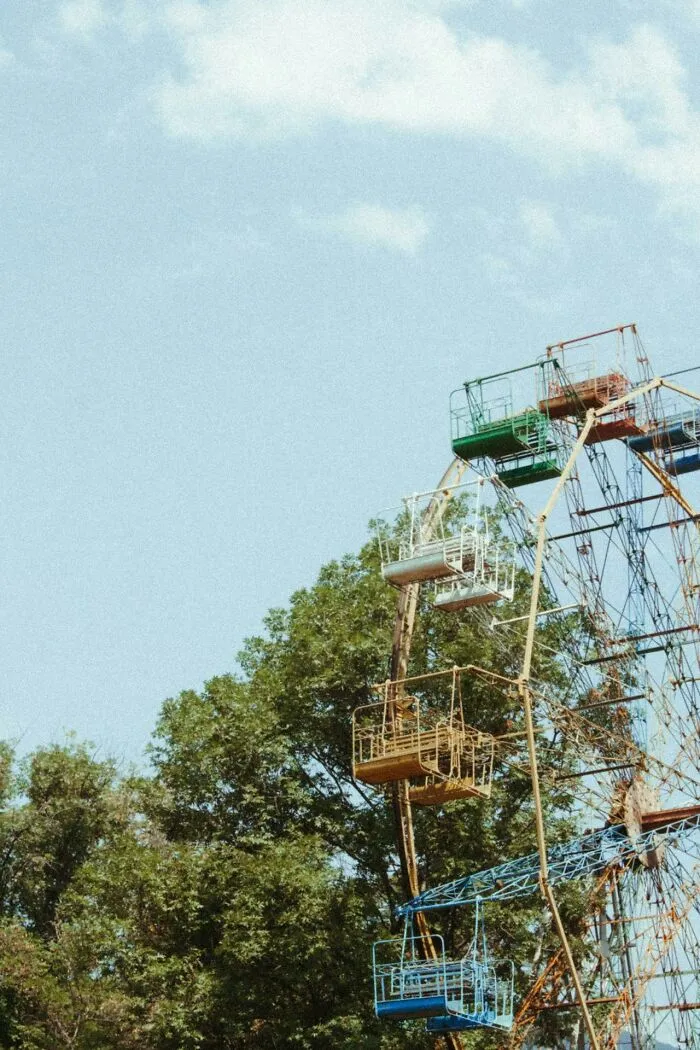 Rusty Ferris wheel with faded colorful seats surrounded by trees, evoking bizarre and creepy park ranger sightings.