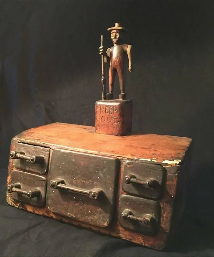 Very old wooden object resembling a stove with a carved figure saying Keep Out, showing ancient objects of ancestors.