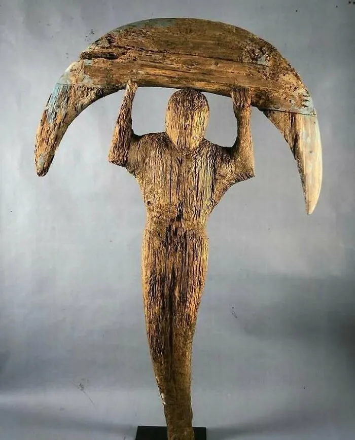 Wooden sculpture of a very old object depicting a human figure holding a crescent shape from ancient ancestors.