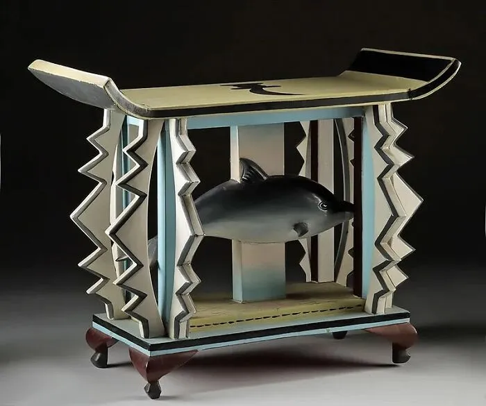 Antique wooden stool with carved zigzag patterns and a fish sculpture, a very old object showing stories about ancestors.