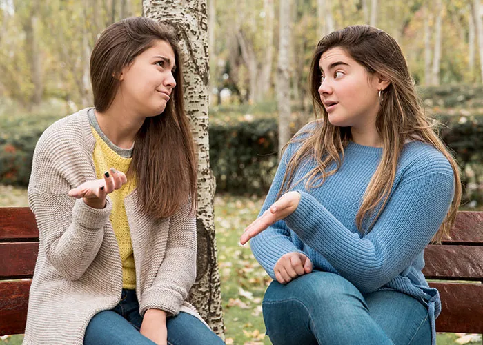 Two young women sitting on a bench in a park using psychological tricks during an engaging conversation on a fall day.
