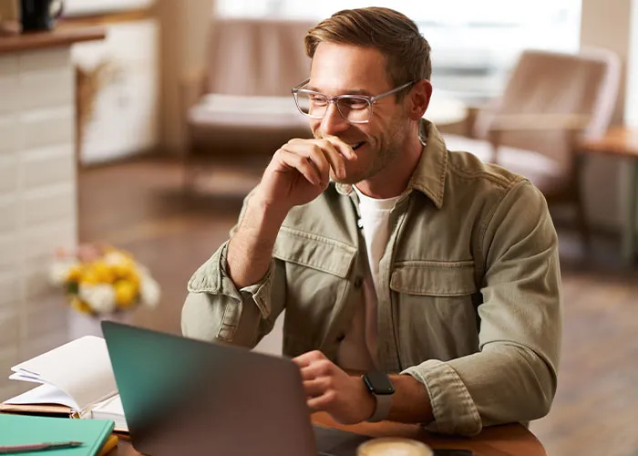 Man with glasses using laptop at home smiling while applying psychological tricks on himself and others that work