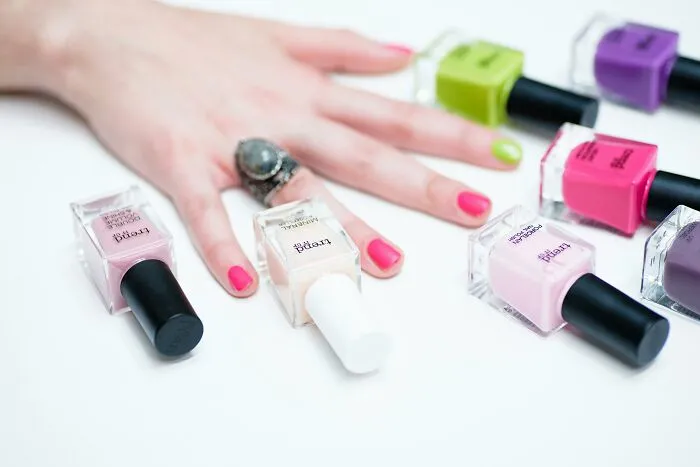 Hand with colorful painted nails surrounded by nail polish bottles showing relationship gestures and princess treatment.