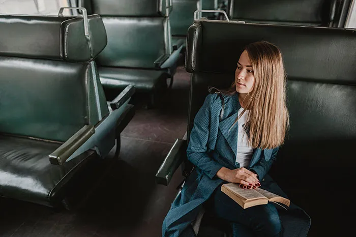 Mujer pensativa en un tren vacío sosteniendo un libro, reflejando el impacto de vivir con mentiras contadas.
