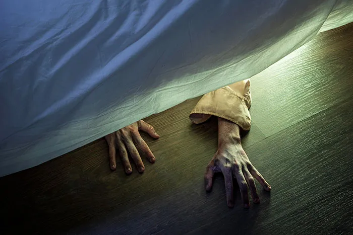 Hands with long fingers reaching out from under a bed, creating a scary and eerie waking up scenario.