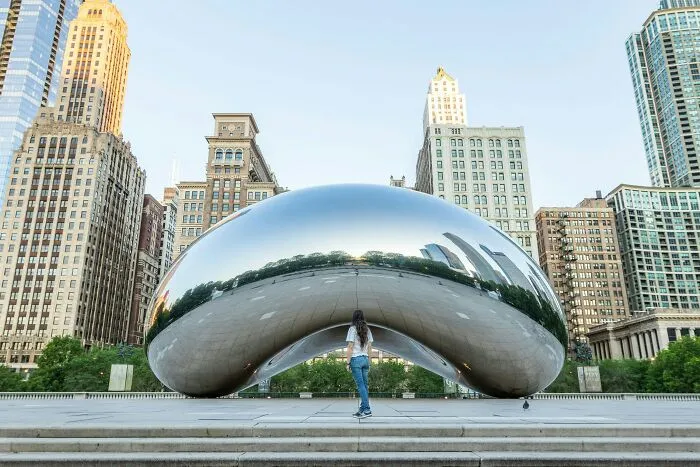 Woman standing in front of a spectacular reflective sculpture in the cityscape, a must-see travel bucket list destination.