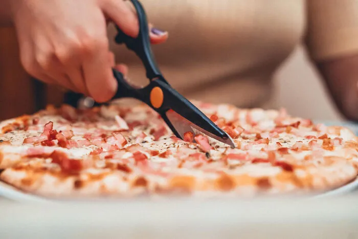 Person cutting a pizza with scissors, one of the most bizarre things people ever seen through a neighbor’s window.