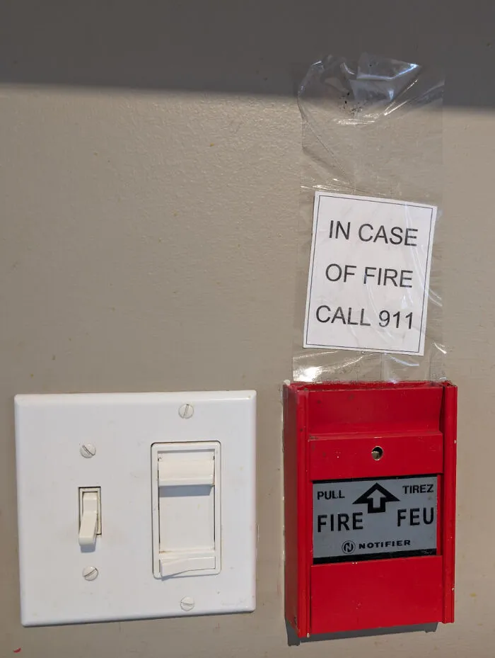 Fire alarm with taped sign to call 911 and light switches on a wall, illustrating rental nightmares and landlord shortcuts.