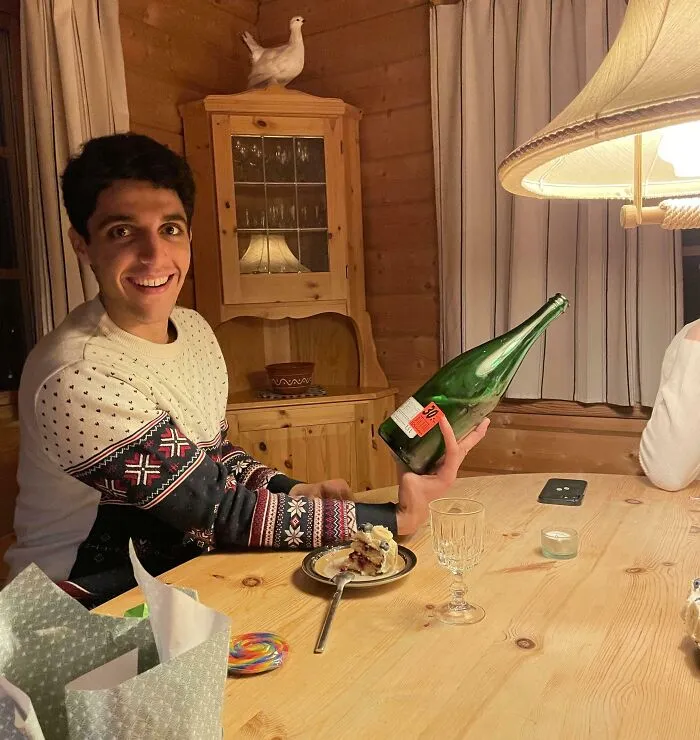 Young man in a cozy room holding a large green bottle at an angle, creating a confusing photo for the brain to catch up.