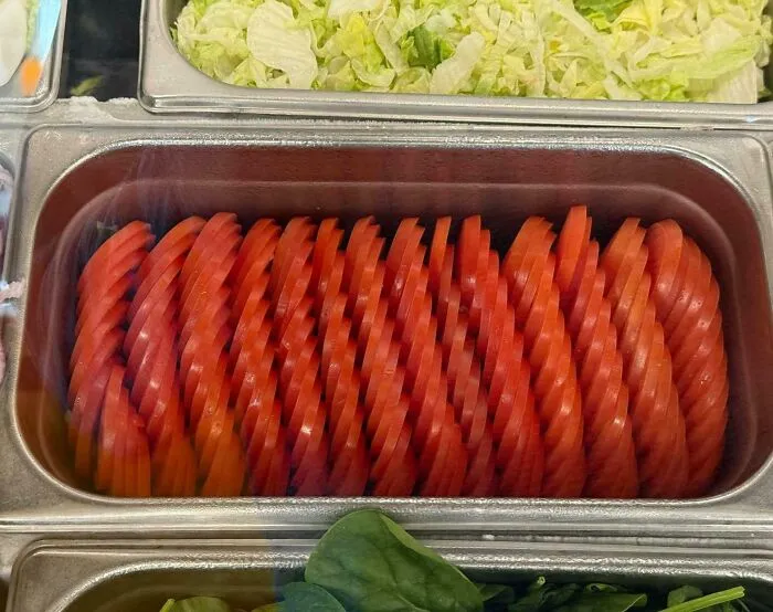 Close-up of a container with tomato slices arranged in a way that looks visually confusing and challenging to catch up.