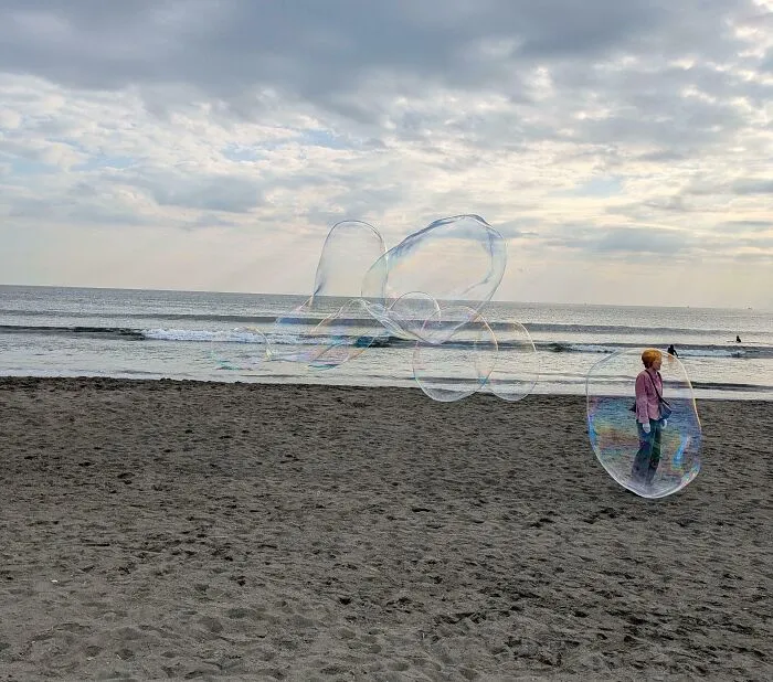 Person on beach inside giant transparent bubble, with several large bubbles floating above the sand, confusing photo effect.