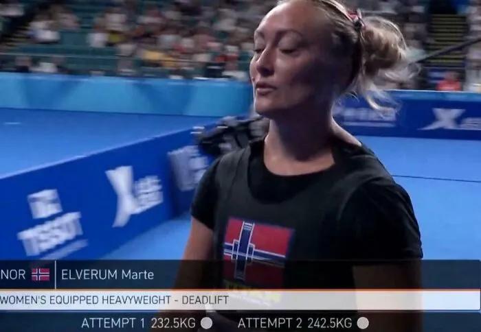 Woman athlete preparing for heavyweight deadlift attempt in sports arena, showcasing smart and cool design in athletic gear.