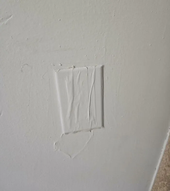Wall with a poorly patched outlet cover showing a rental nightmare where landlords cut corners on repairs.