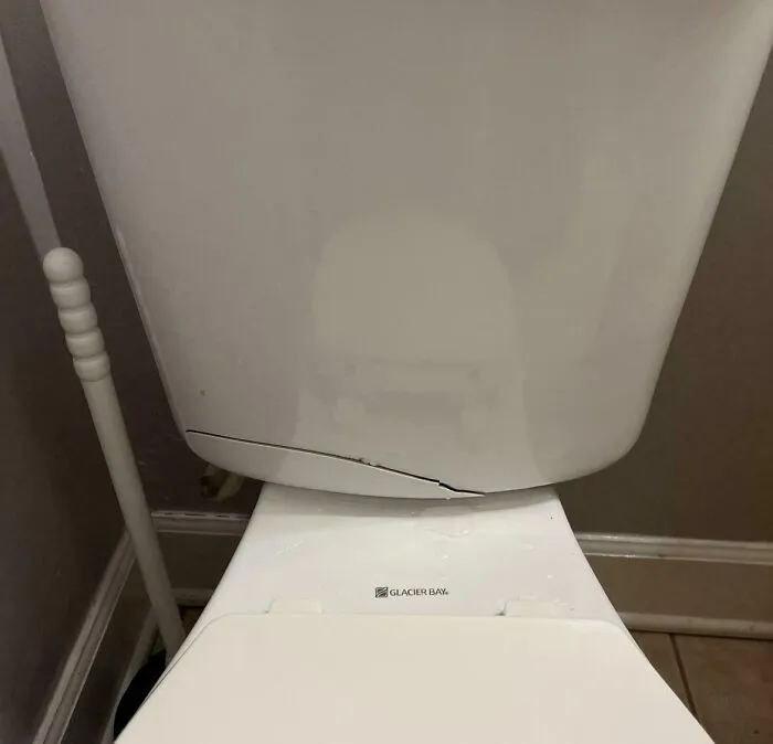 Toilet tank with a visible crack at the bottom, illustrating rental nightmares where landlords cut corners and caused damage.