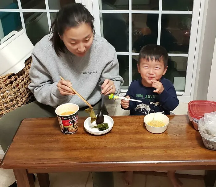 Woman and smiling child sharing a meal at a table, capturing a heartwarming moment that brightens the day.